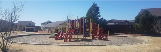 An image of a playground. The playground is red and yellow with slides, climbing ladders, and stairs. There are trees and grass surrounding the playground.
